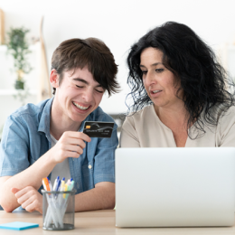 Parent and teen looking at credit card together in front of laptop at home