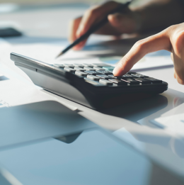 Hand clicking button on calculator while other hand is holding pen to financial papers in background