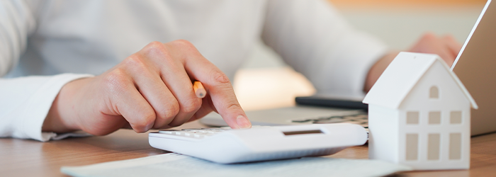 Person's hand clicking button on calculator with ceramic home figurine and laptop in background