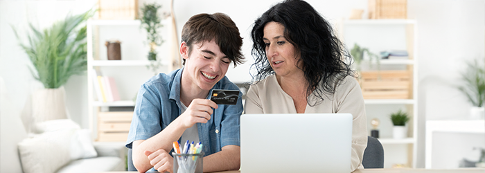 Parent and teen looking at credit card together in front of laptop at home