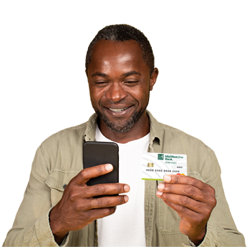 Male with dark skin and black hair wearing green jacket looking at phone holding MidWestOne Bank debit card