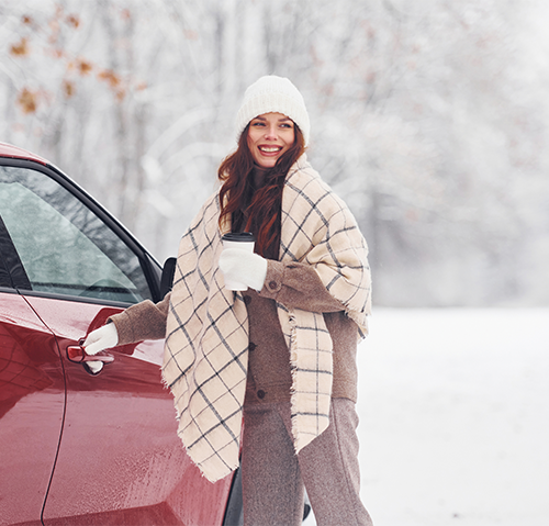 middle age woman holding a coffee cup and opening door of red car